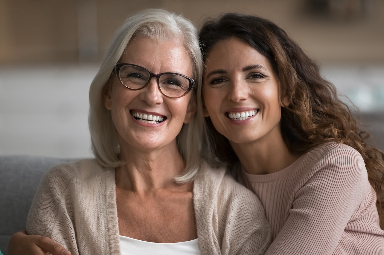 Smiling middle-aged and younger woman sitting together at home, symbolising women’s health and wellbeing at different life stages.